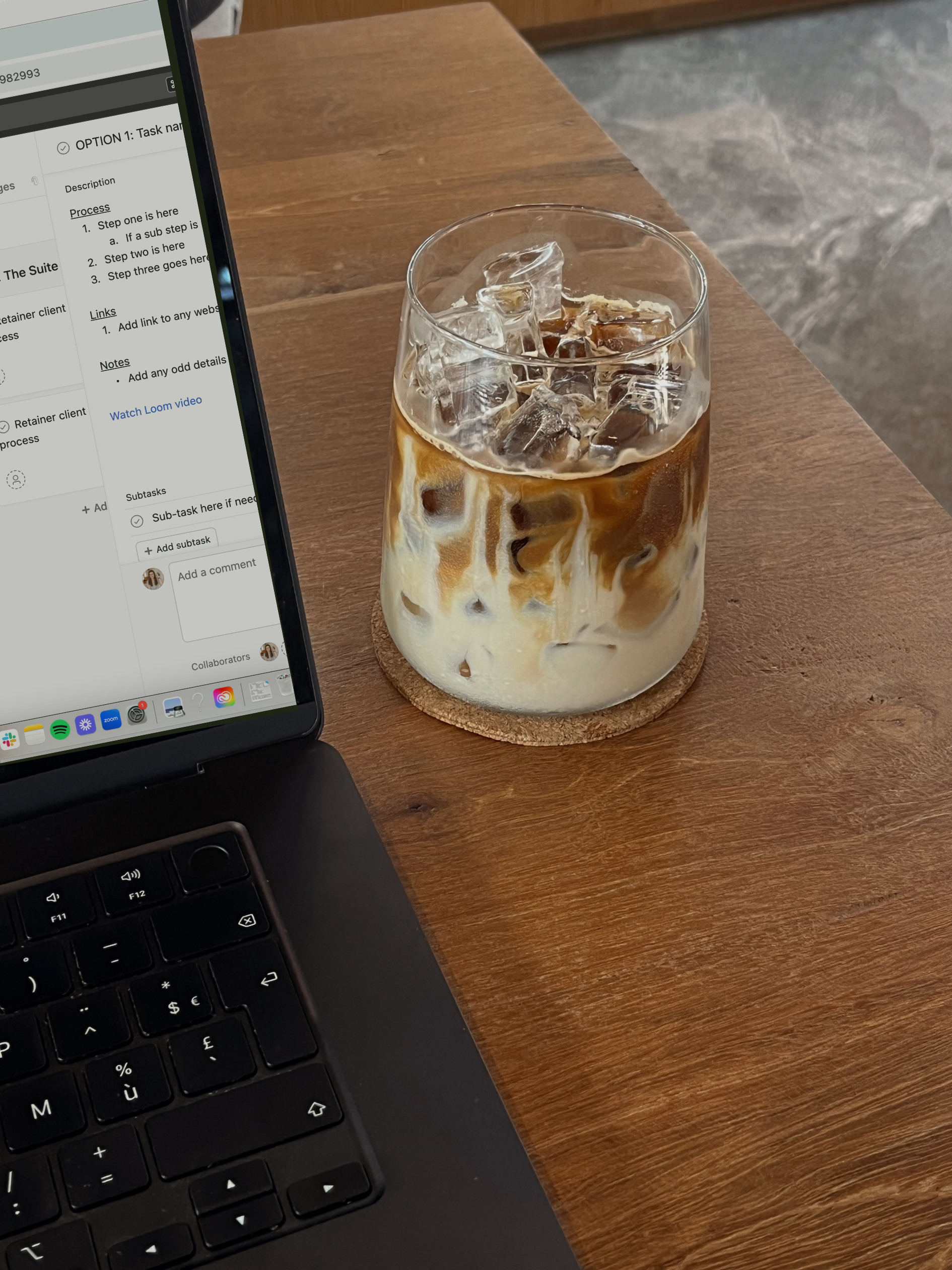 Iced coffee on wood table next to laptop with Asana on the screen